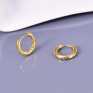 Macro shot of polished gold-plated stainless steel hoop earrings on a reflective surface