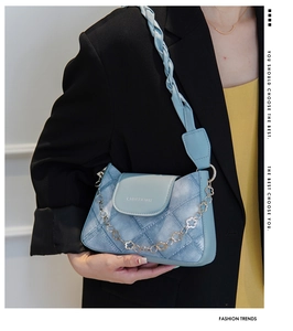 Detail of blue denim textured underarm bag featuring a metallic floral chain and woven strap