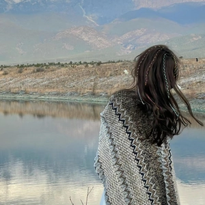 Ethnic knit shawl with wave patterns and tassels worn by a lake against mountain scenery
