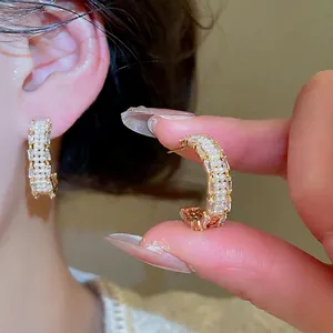 Gold plated C-shaped earrings with pearls and emerald cut zircons on a model