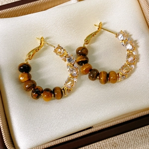 Detailed close-up of gold hoop earrings with tiger's eye stone and crystals in a jewelry box