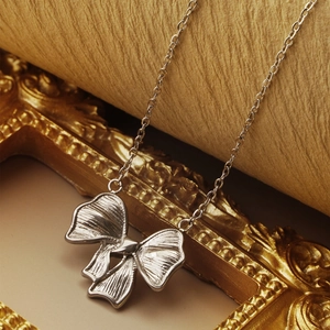 Elegant silver bow pendant necklace displayed on a vintage golden frame background