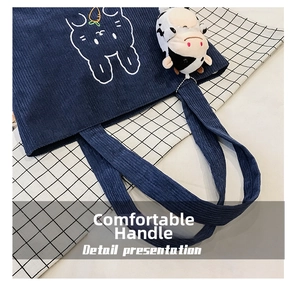 Detail of dark blue corduroy tote bag with white rabbit embroidery and cow plush charm