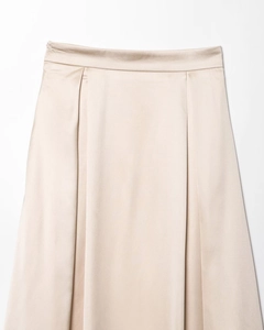 Détail d'une jupe mi-longue en satin champagne montrant la texture et les plis à la taille