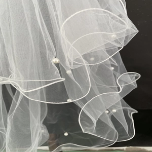Detail of white bridal veil featuring layered mesh fabric with pearl bead accents and curly edges