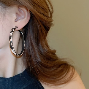 Detail shot of a model wearing large leopard print hoop earrings with a textured leather finish