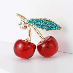 Cute red cherry brooch with golden leaves and sparkling rhinestones on white surface