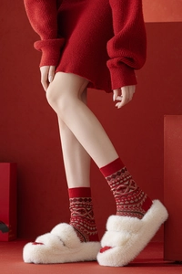 Détail de chaussettes en laine rouge avec motifs de flocon nordique et pantoufles blanches