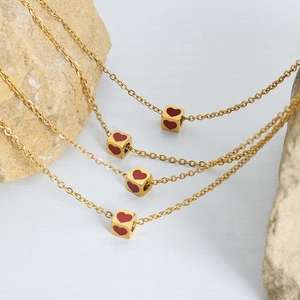 Minimalist gold necklace with red heart square pendant displayed on natural stone