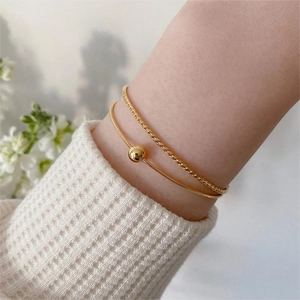 Detailed close-up of double-layered gold snake chain bracelet with round bead on wrist