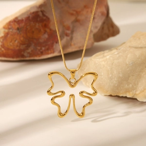 Macro shot of gold butterfly hollow pendant on snake chain over natural rock