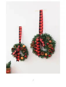 Detail of Christmas wreaths with pine cones, red berries and plaid bows on white wall