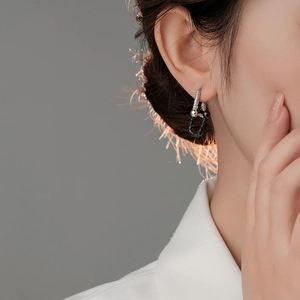 Detail of model wearing u-shaped two-tone black and silver horseshoe chain earrings