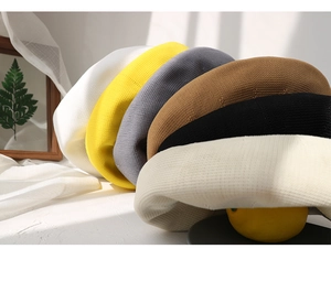 Detail view of knitted beret hats in white, yellow, gray, and khaki stacked together