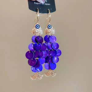 Detail of fish-shaped shell earrings with purple sequins and evil eye charm