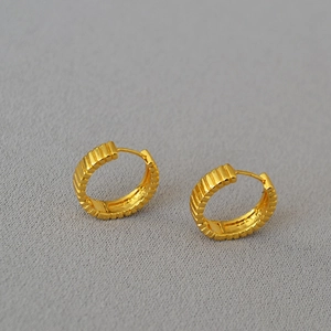Dettaglio macro di orecchini a cerchio in ottone dorato con eleganti strisce verticali