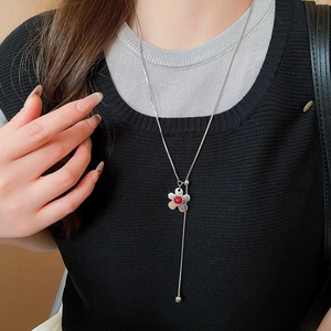 Close-up of silver flower necklace with red center and Y-shaped tassel on a model