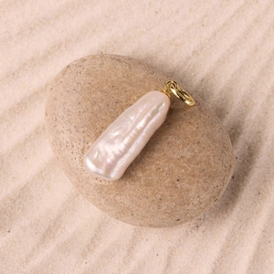 Macro view of white baroque pearl pendant with gold metal clasp on natural pebbles