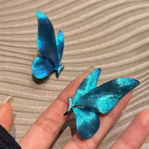 Elegant blue butterfly earrings with metallic texture and small diamonds in a hand view