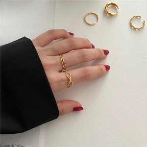 Detail shot of gold minimalist twist rings styled with professional black blazer and red nails