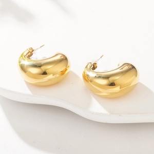 Detail of chunky gold C-shape stud earrings with polished mirror finish on white stand