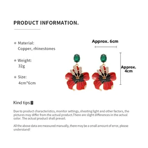 Détails des boucles d'oreilles fleurs aux pétales rouges, gemmes vertes et strass