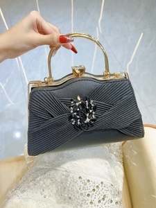 Detail of black pleated fabric evening bag with a crystal flower clasp and gold handle