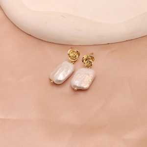 Macro shot of gold rose earrings featuring rectangular baroque pearls on pink silk fabric