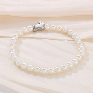 Detail of pearl bracelet featuring a silver pig charm on elegant silk fabric background