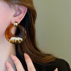 Detail view of large resin tortoise shell hoop earring with gold leopard emblem on model