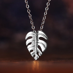 Macro shot of silver monstera leaf pendant with polished mirror finish on a dark wood surface