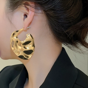 Close-up of woman wearing oversized golden lava-textured geometric metal earrings