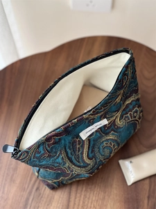 Macro view of blue paisley jacquard cosmetic bag with gold embroidery and zipper detail