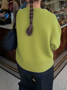 Detail view of the ribbed hem and back fit of a yellow-green crewneck knit sweater