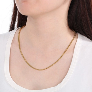 Detail van een goudkleurige visgraatketting gedragen op een witte top