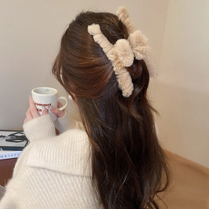 Close-up of a plush cross claw clip in beige, showing soft texture and hair styling effect