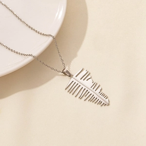 Macro detail of silver leaf pendant necklace on ceramic plate with a cross chain