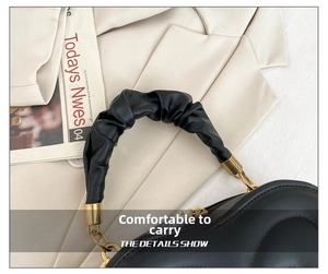 Detail of black pleated handle handbag with elegant gold metal hardware and stitching