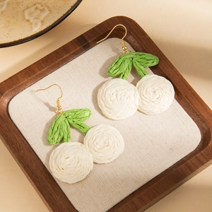 Detail of handmade woven cherry earrings with white crochet balls and green leaf accents