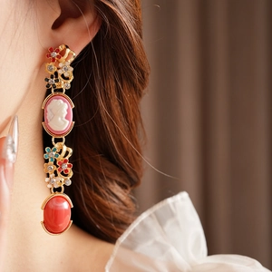 Close-up of vintage gold earrings with pink cameo, colorful enamel flowers and red gems
