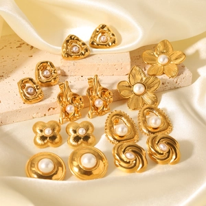 Golden flower and geometric pearl earrings set displayed on a beige stone pedestal