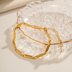 Detailed close-up of a 18K gold plated rhombic link necklace with lobster clasp on glass