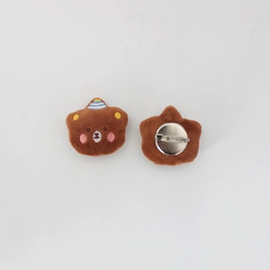 Detail of brown plush bear brooch showing front embroidery and metal pin closure