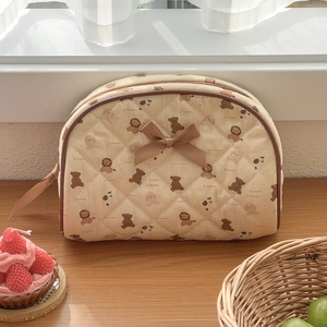 Close-up of quilted beige makeup bag with brown bear patterns and decorative ribbon
