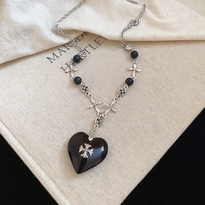 Detail of Gothic black heart pendant with silver cross crest on vintage chain necklace