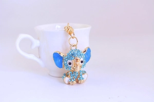 Close-up of elephant keychain with blue rhinestones hanging on a white ceramic cup