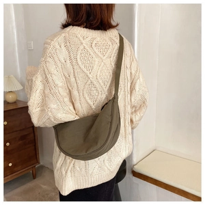 Detail of army green nylon half-moon crossbody bag worn over a beige knit sweater