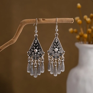 Detail of vintage silver bohemian tassel earrings hanging on a natural wooden branch