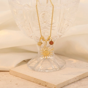 Detailed close-up of gold necklace with sun, star and bead charms on a crystal glass