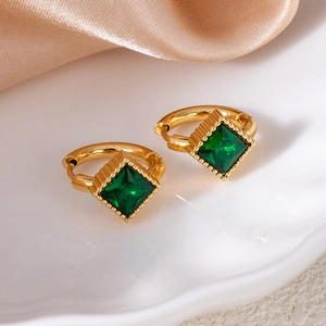Macro view of gold hoop earrings featuring square emerald zircon pendants on silk